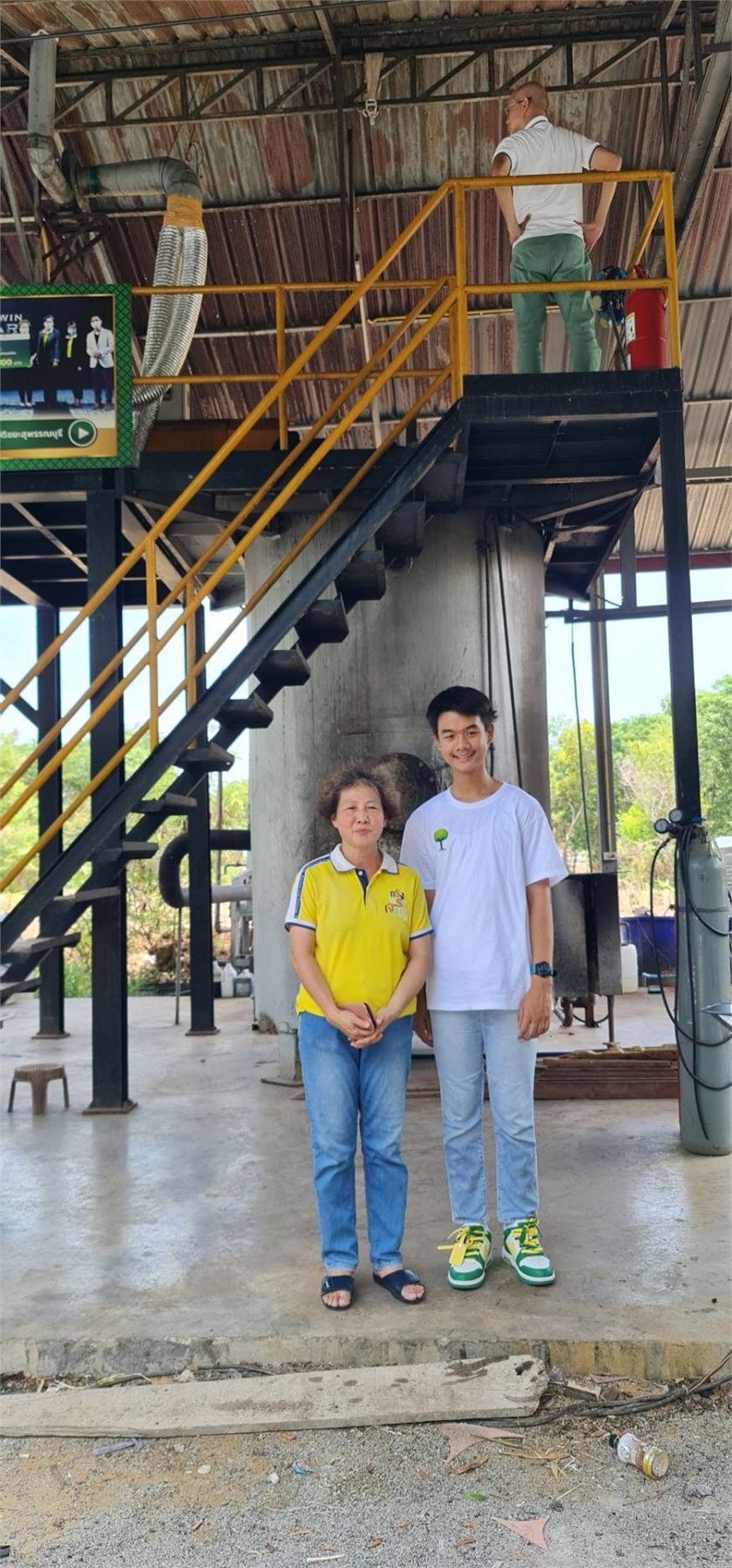 Two people standing in front of a plastic waste-to-fuel plant